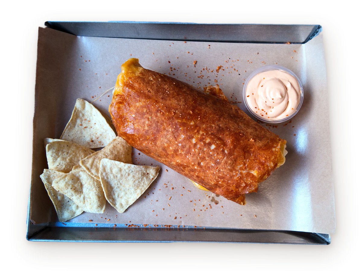 Nachoz cheese crusted burrito on a tray with tortilla chips and a dip, seen from above